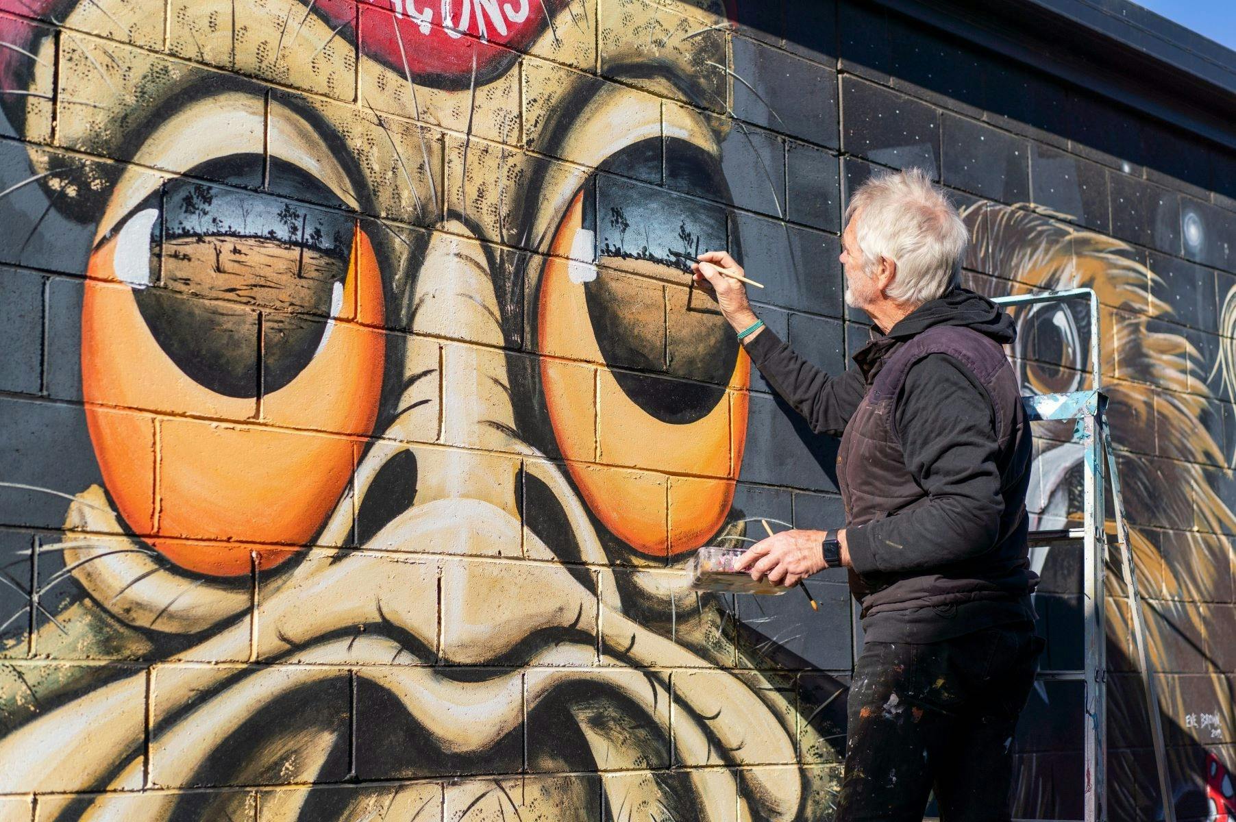 John Murray paints one of his iconic emu figures on a wall