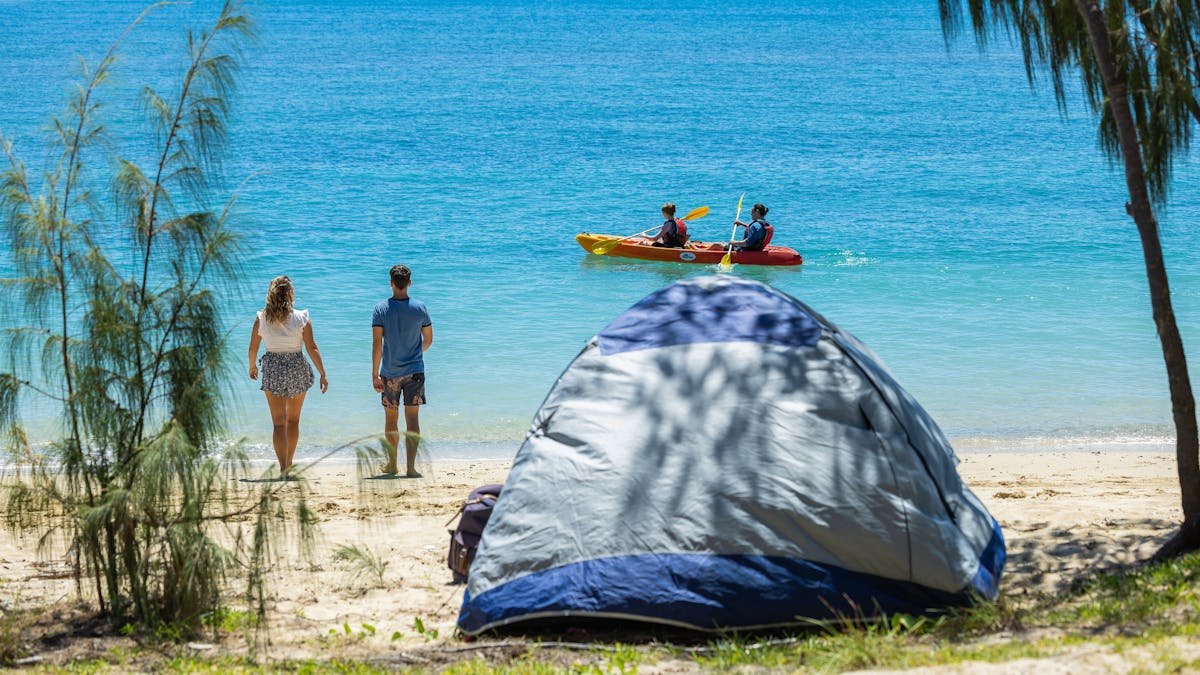 View from the beach of tent with two people walking on the beach and people kayaking in distance