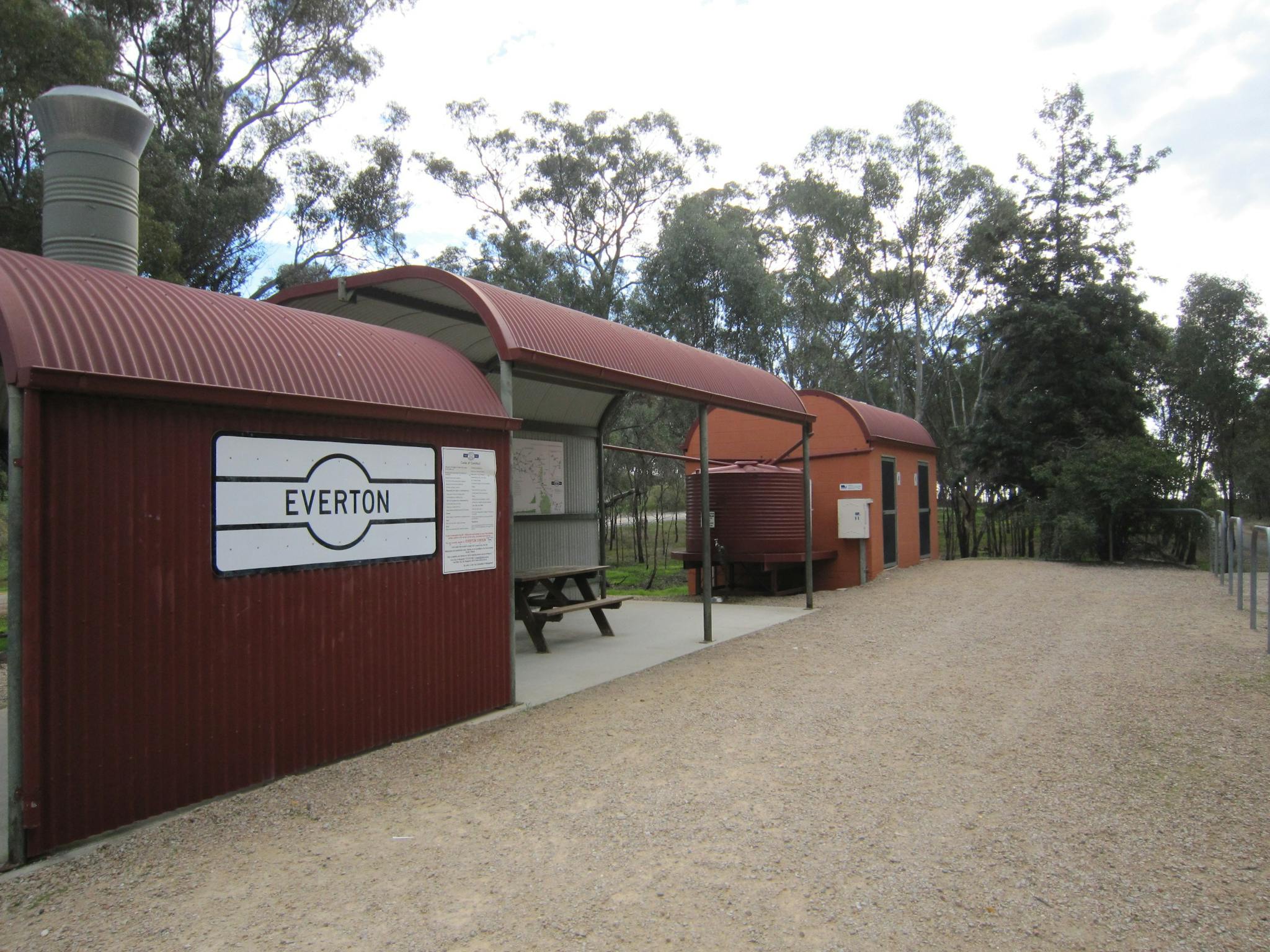 rustic shelter depicting a steam train and carriages with picnic table, water tank, and toilets