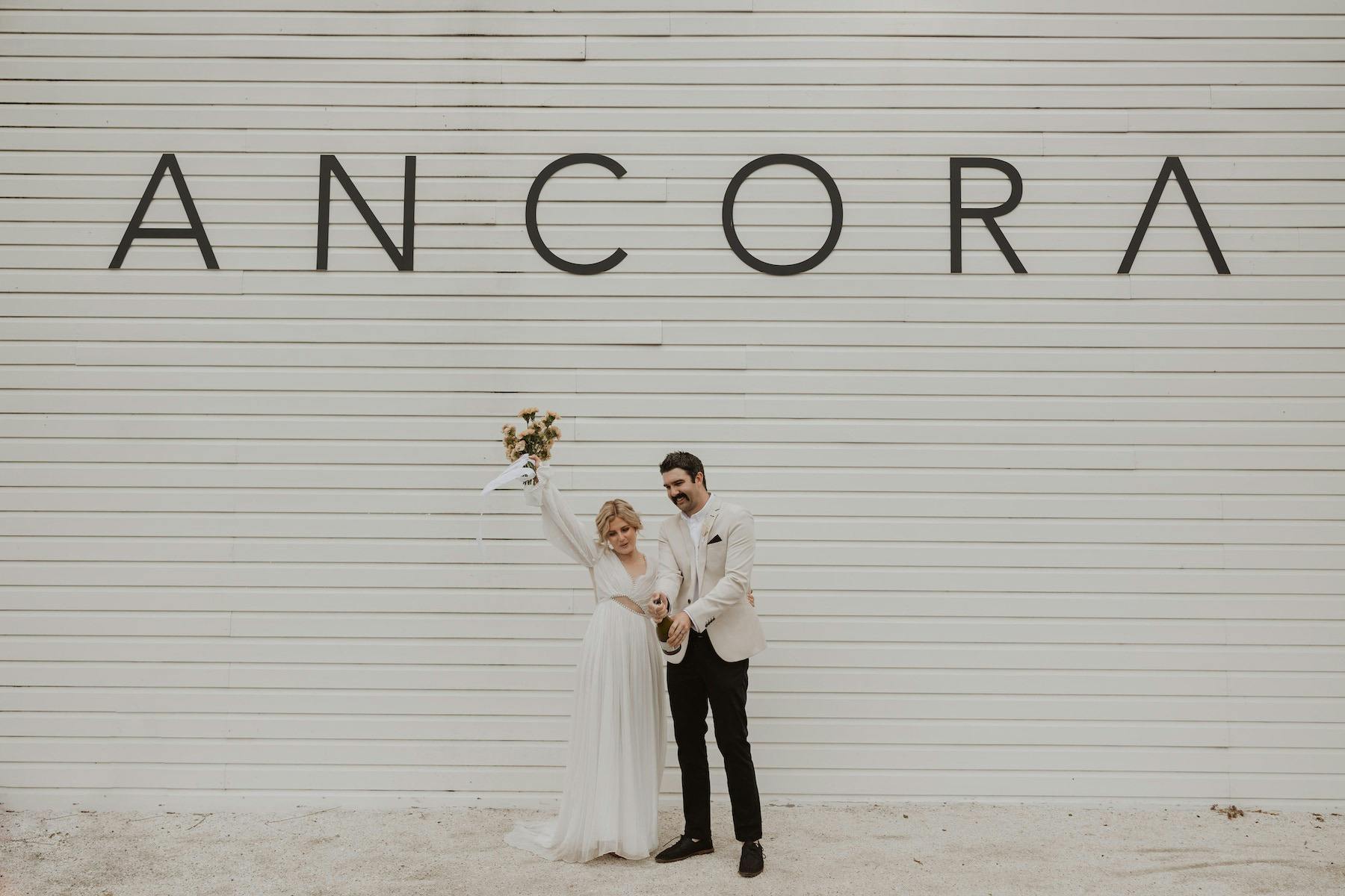 Anna and Corey celebrating in front of the Ancora name wall