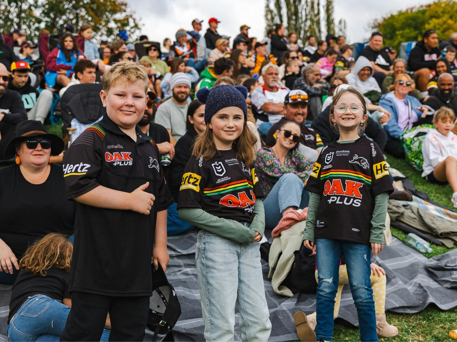 Three kids in the crowd smiling and enjoying the Bathurst NRL match.
