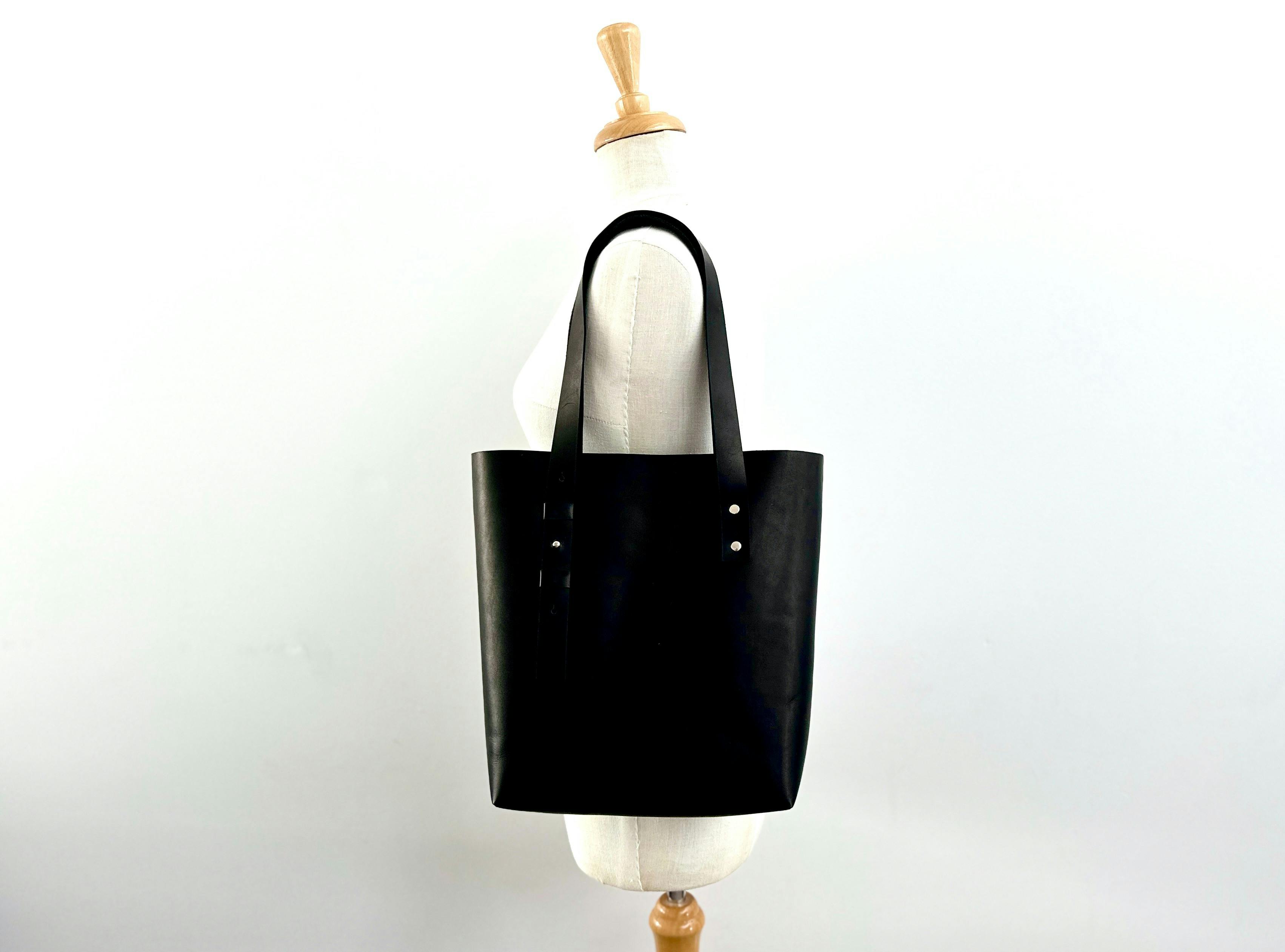 Black handmade leather tote bag displayed on a mannequin against a plain white background