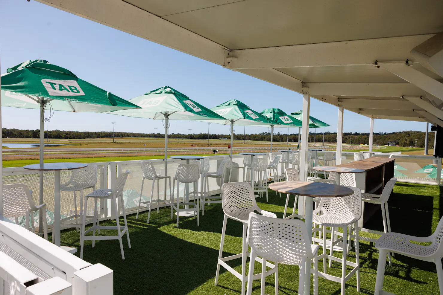 Green TAB Branded umbrellas with high top tables overlooking the track
