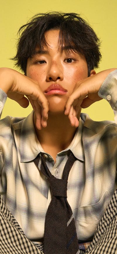 KINKY sitting down with his hands placed under his chin, with a yellow background