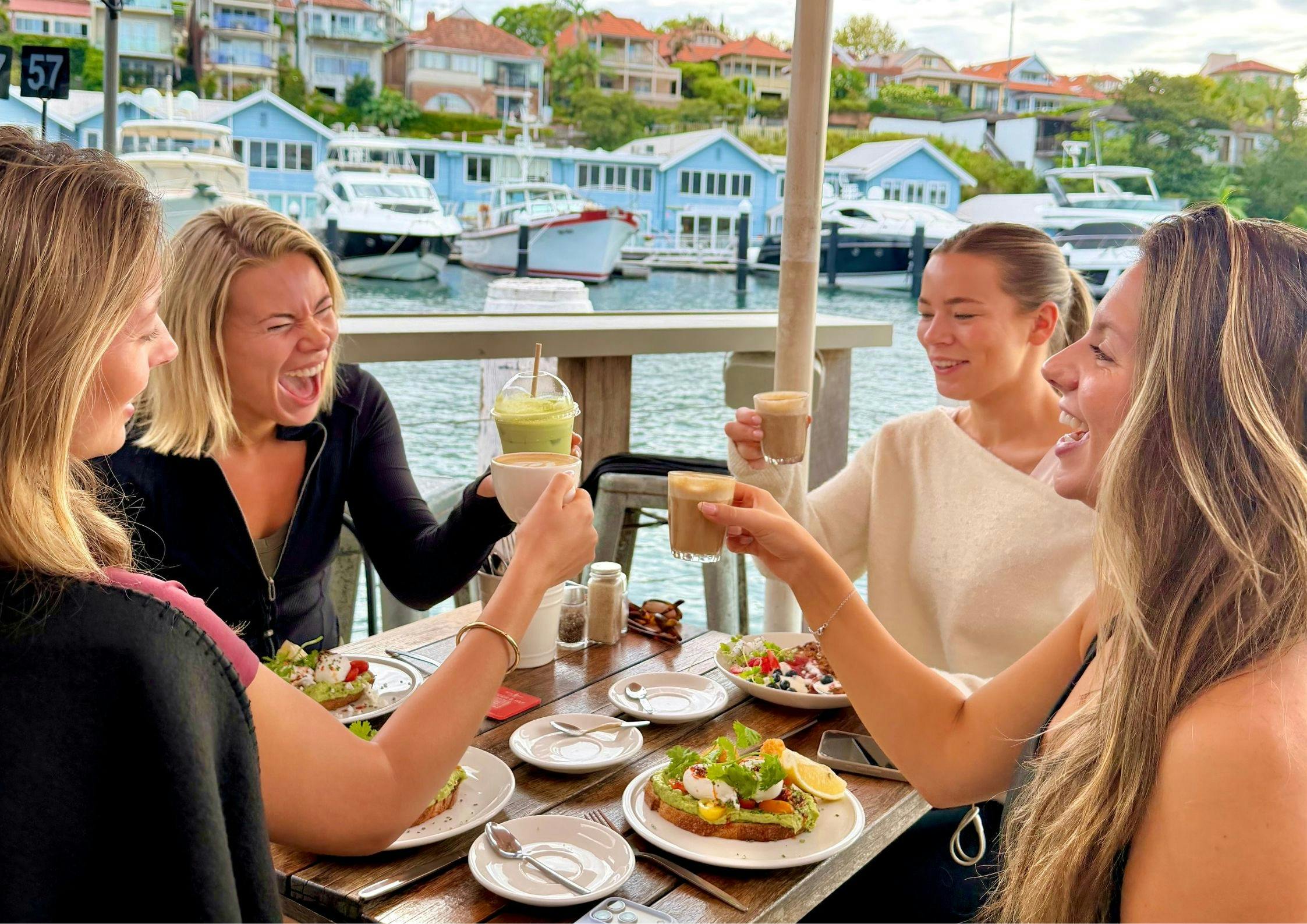 four girls laughing eating breakfast at a waterfront cafe