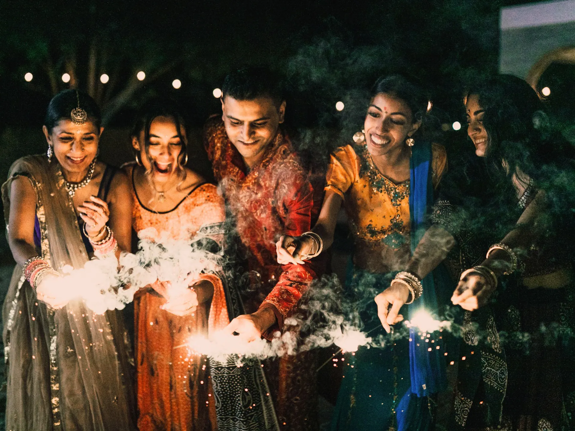 A group of people smiling and having a great time with sparklers in their hands.