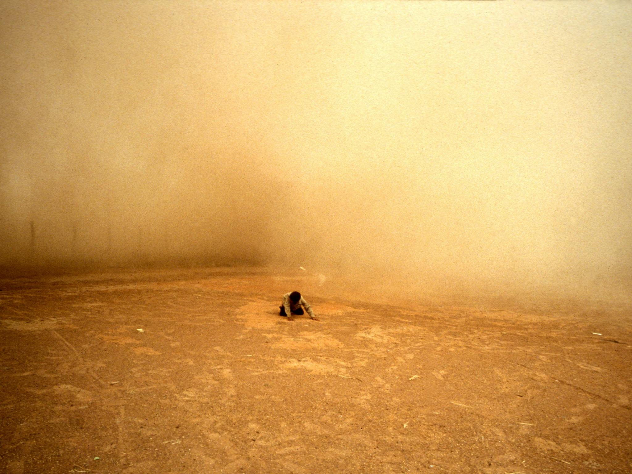 A person in the distance kneeling and looking downwards, surrounded by orage dust A person in the distance kneeling and looking downwards, surrounded by orage dust