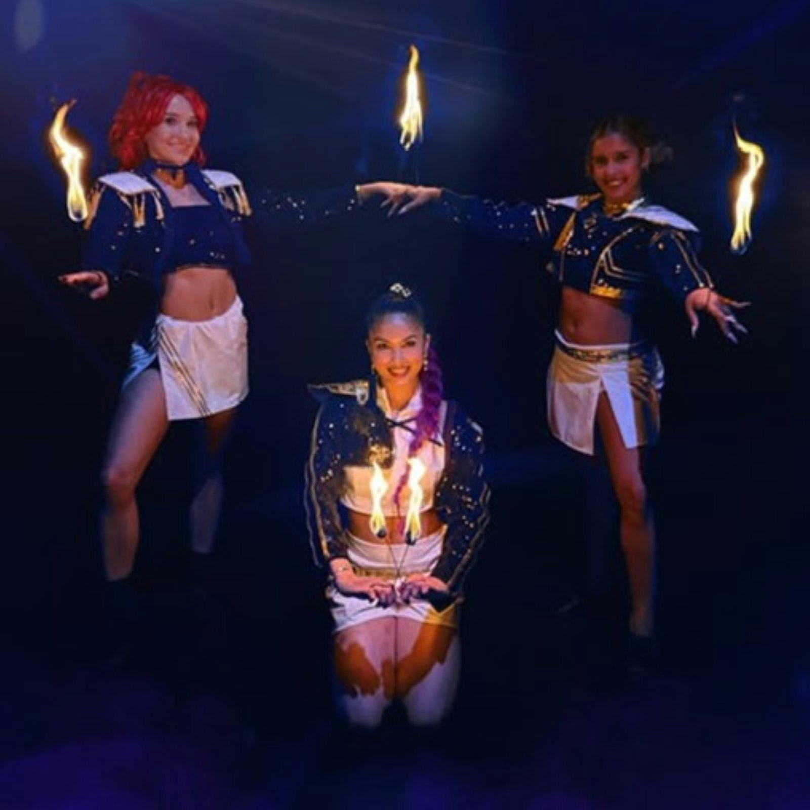 Three ladies 2 standing and one kneeling holding flaming batons