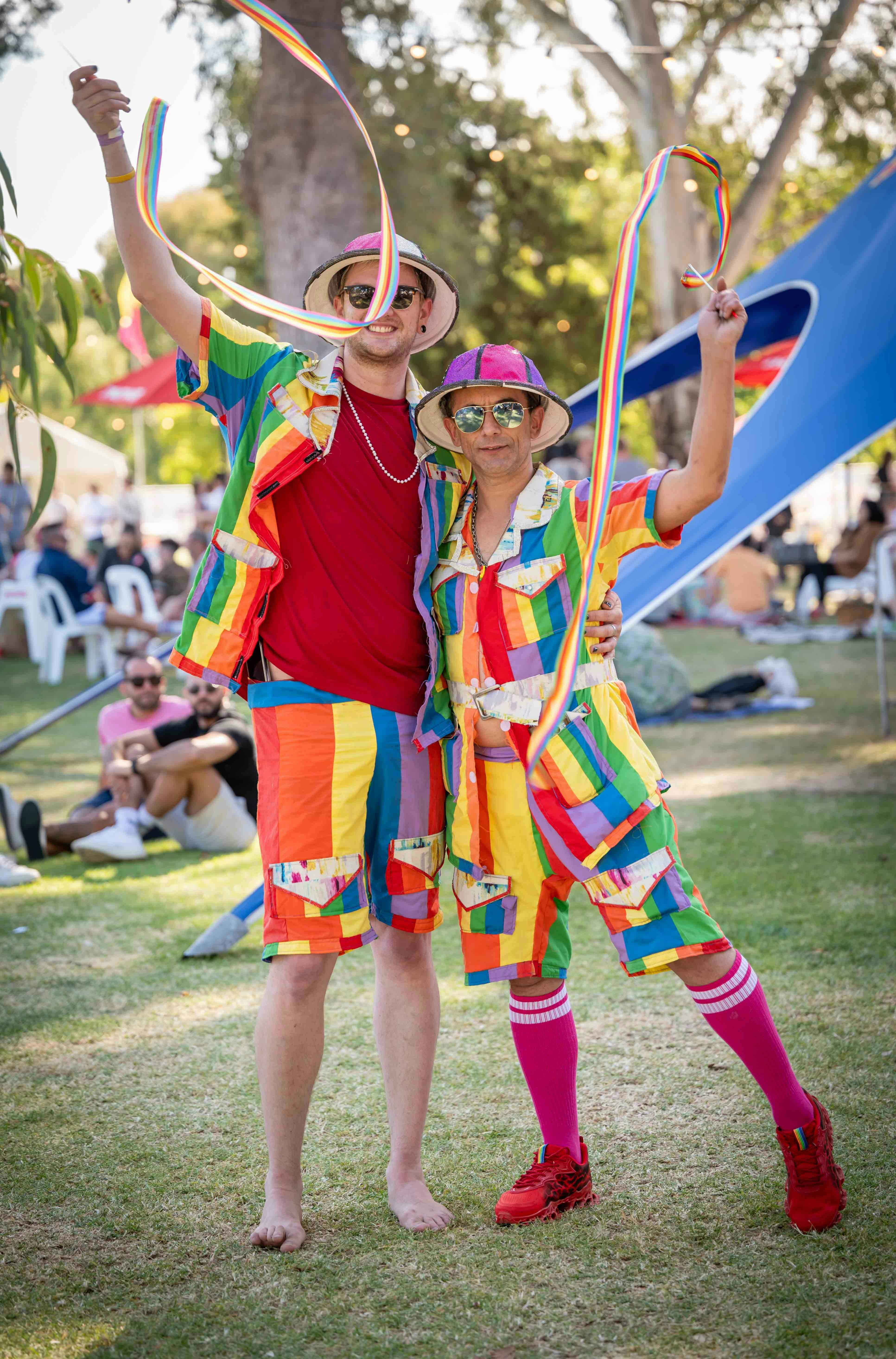 Two people in colourful attire waving rainbow ribbons.