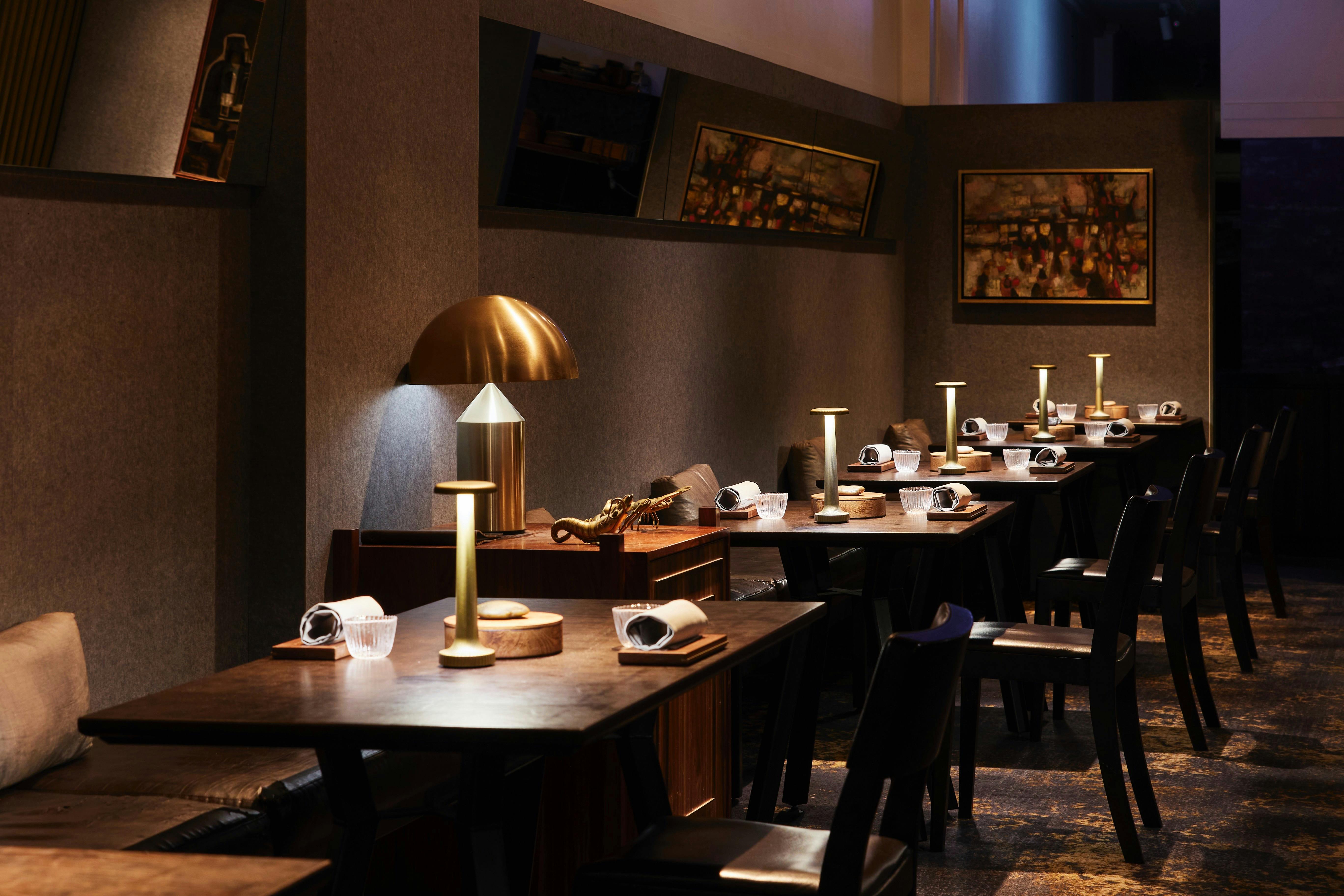 Photo of the dining room at Ides with spacious tables, brass and leather finishes and moody lighting
