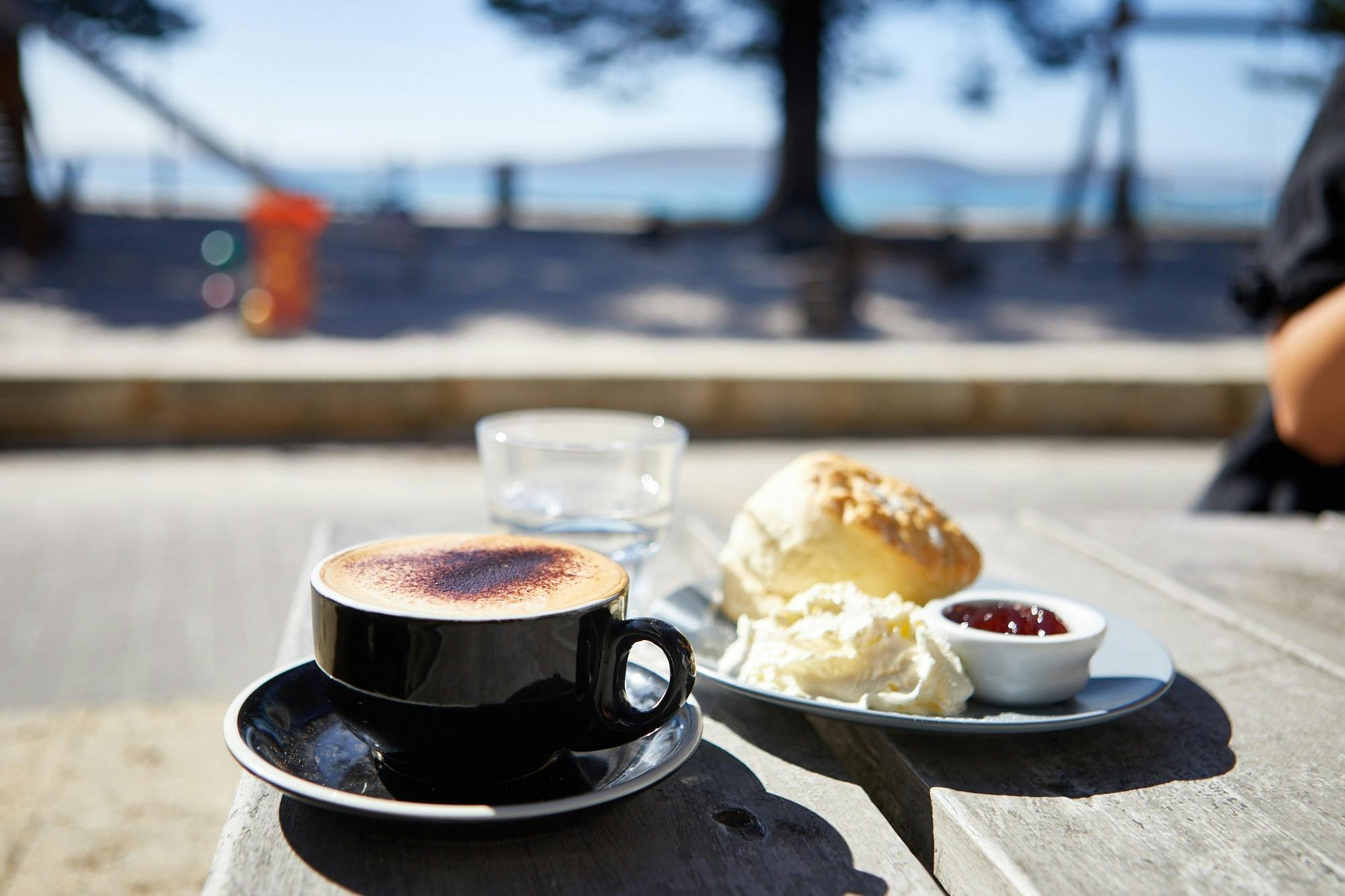 table with view to beach has coffe cup and scone, jam and cream