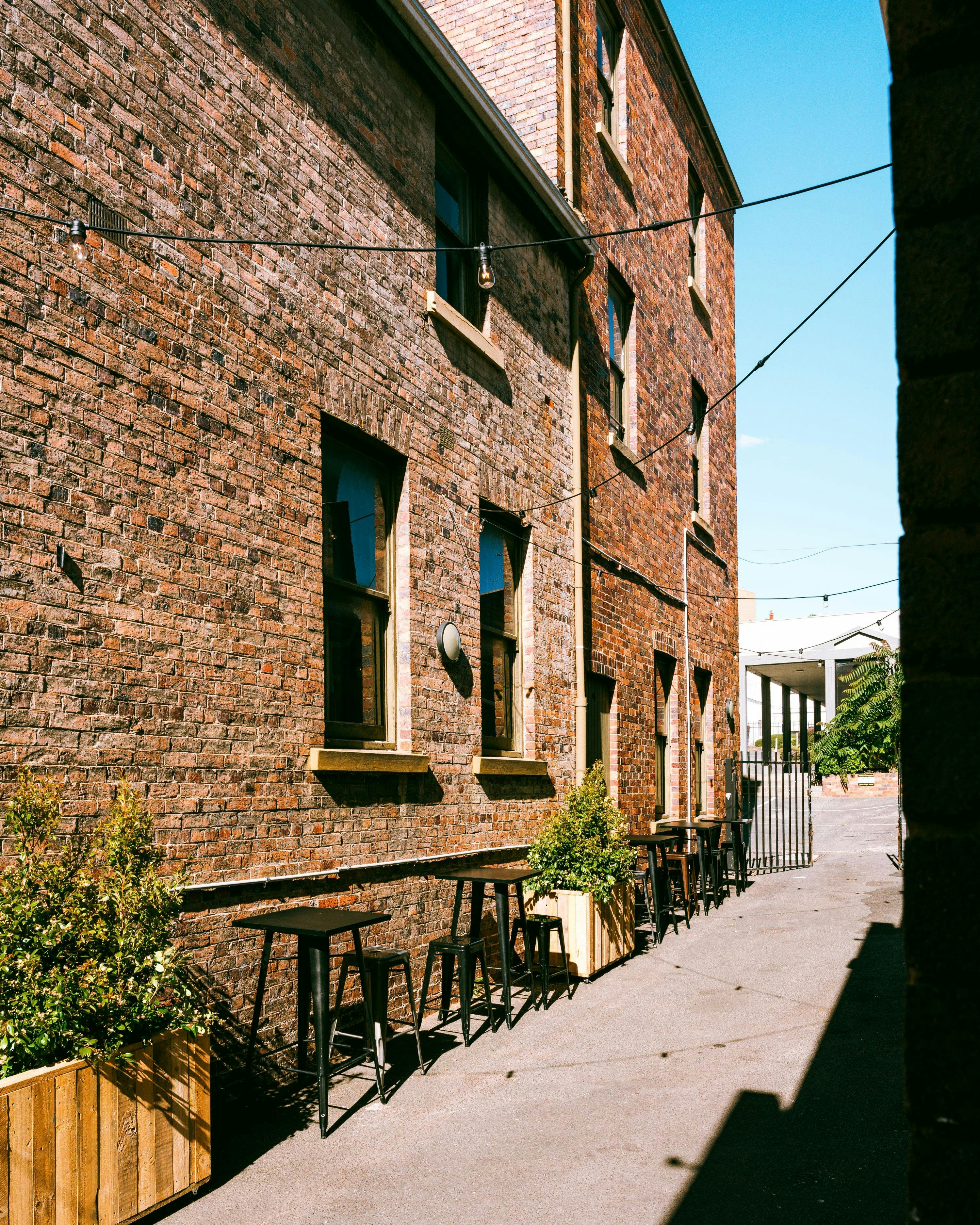 Outdoor laneway seating with high tables beside brick building.