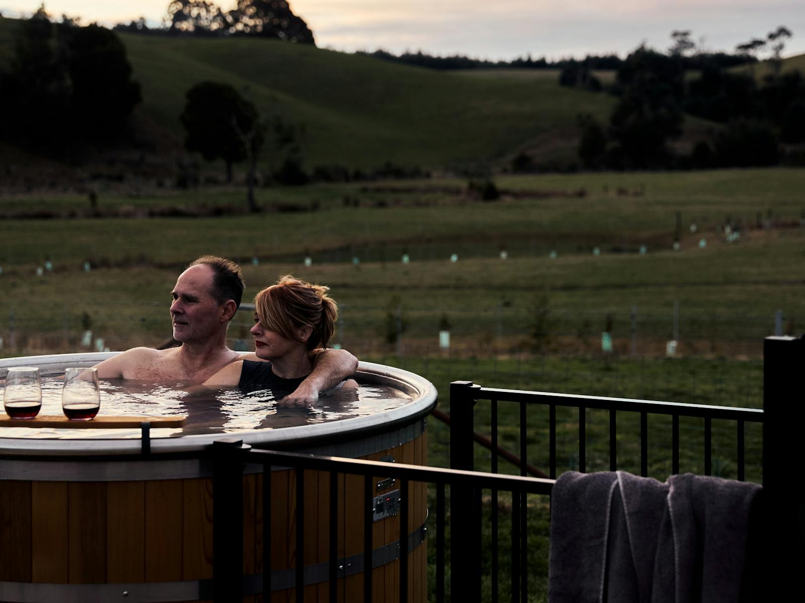man and woman sitting in hot tub with green paddocks behind
