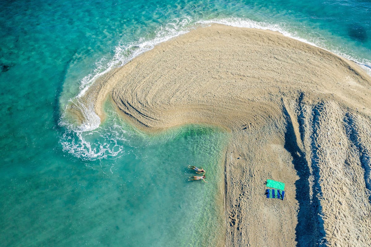 Ariel view of a sand spit curling into tropical blue waters with two swimmers.