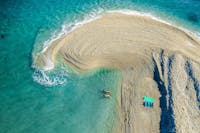 Ariel view of a sand spit curling into tropical blue waters with two swimmers.