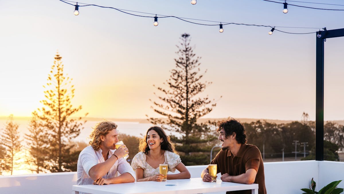 Three people seated at a white table drinking beer