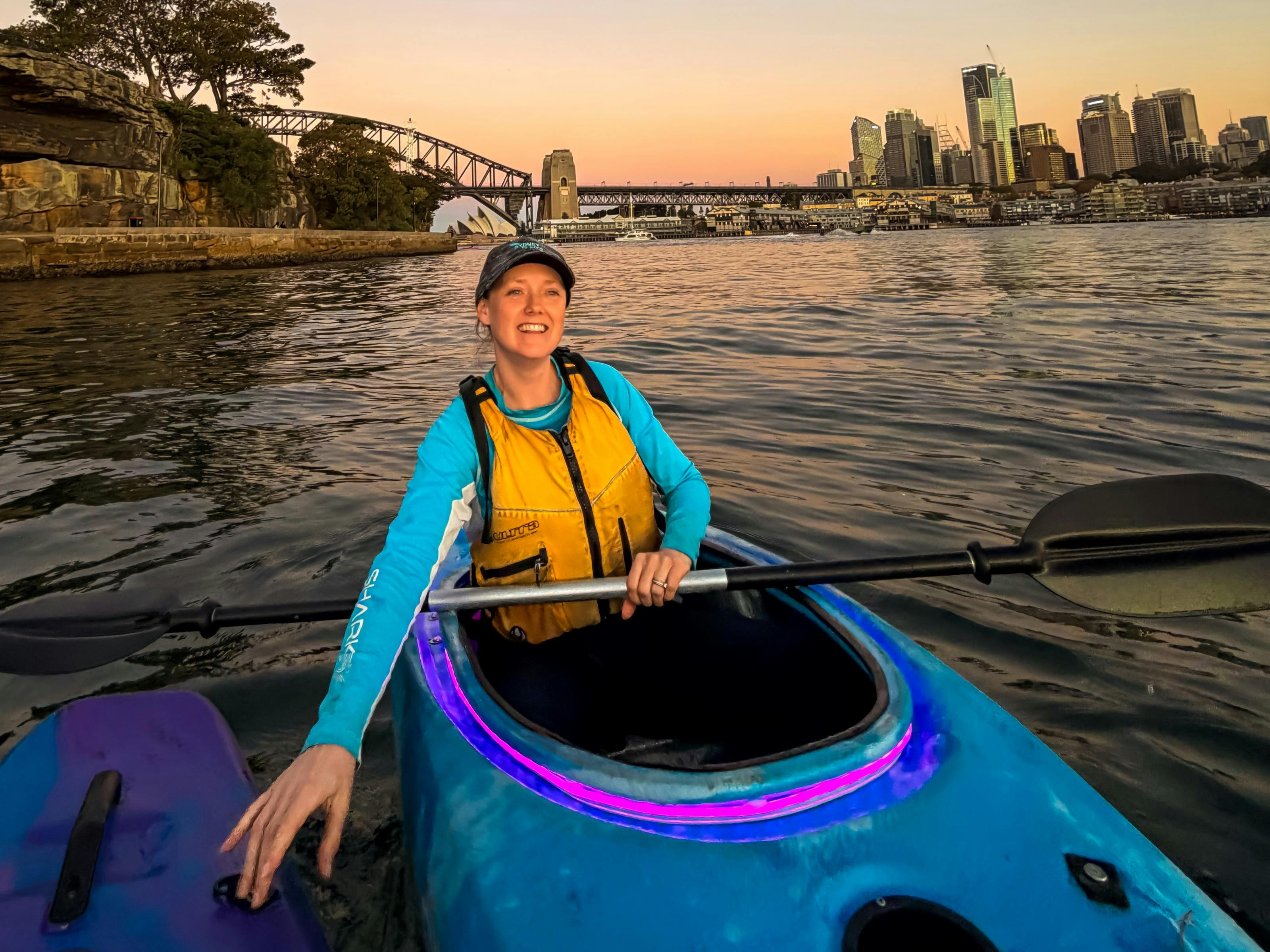 Laura Stone sits in a blue kayak with pink led lights around her kayak on Sydney Harbour.