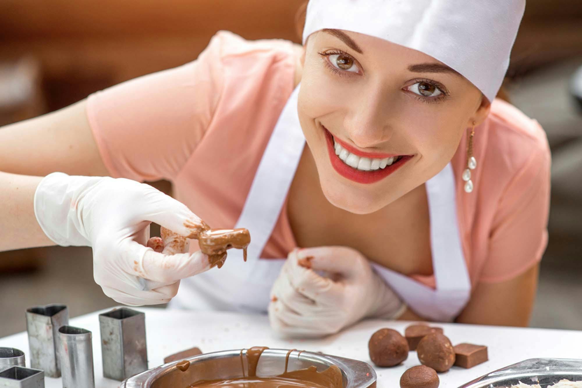 student wearing chef's har and apron dipping ganache into chocolate