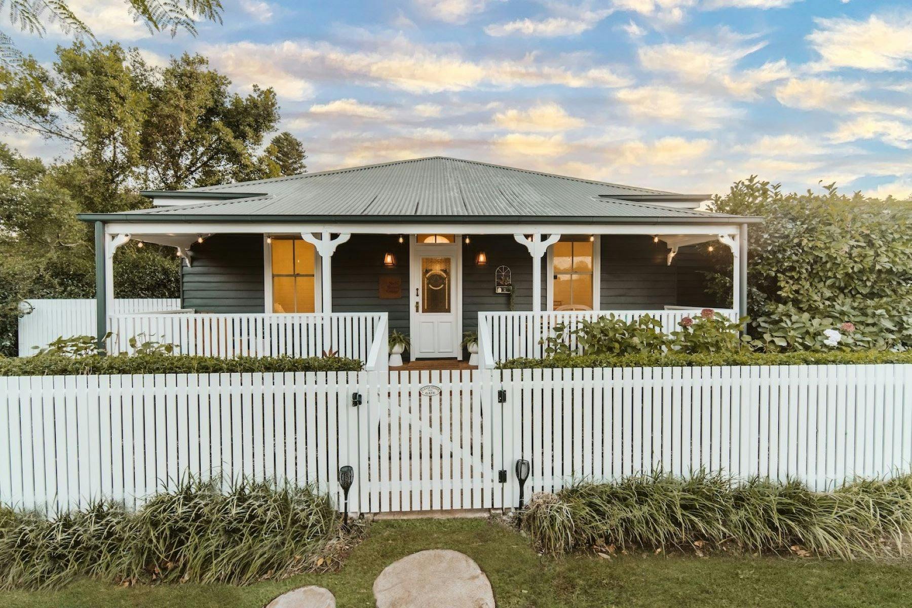 Image of front facade of home. White picket fence surrounds the home.