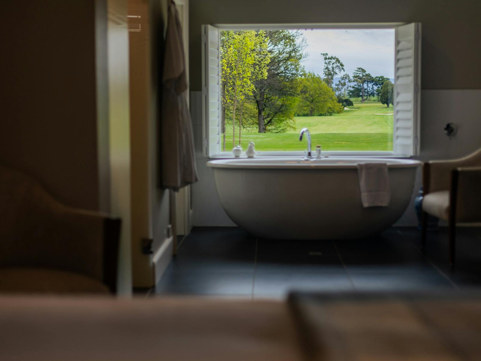 Large egg shaped bath in front of large window overlooking golf course, black tiled floor