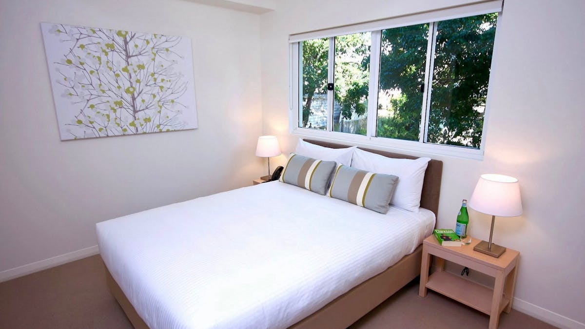 Queen bedroom with white linen, botanical wall art and natural light through a large window at Domai