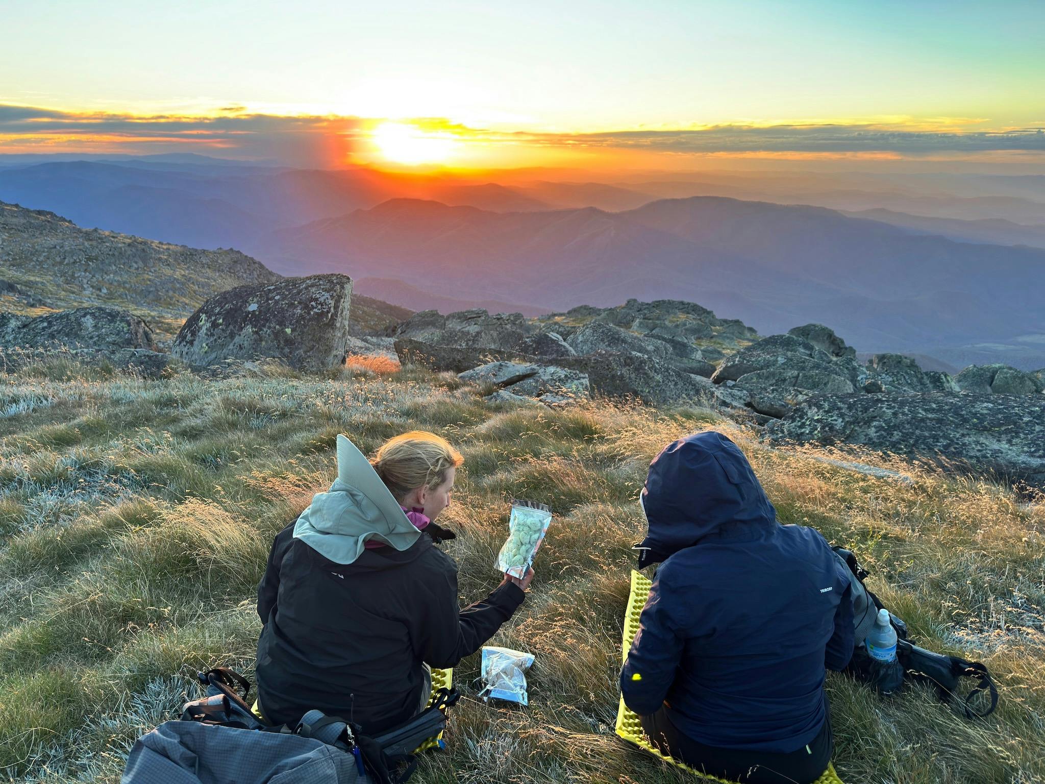 Two hikers watching the sun set and looking at some freeze dried ice cream