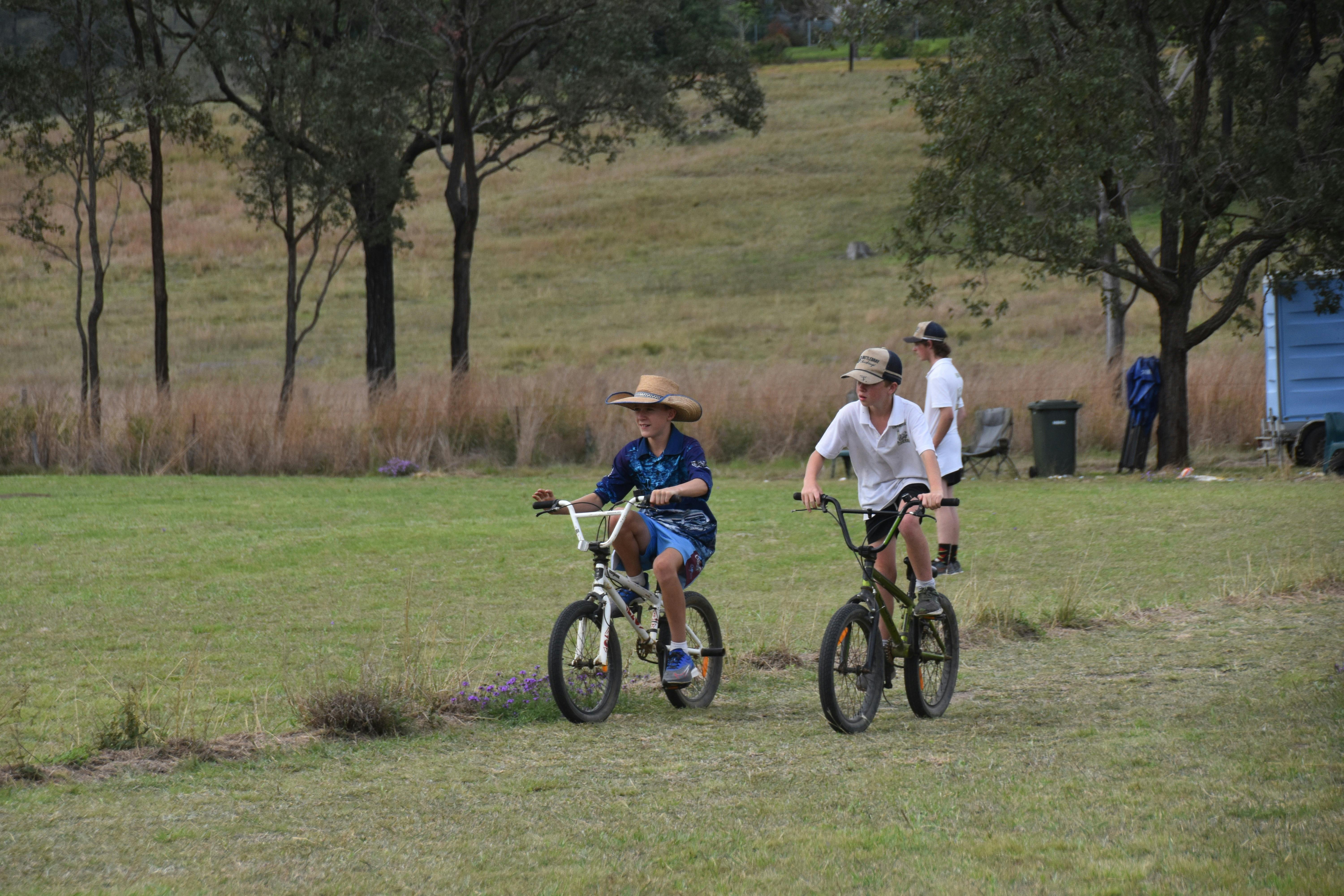 children riding bikes while cricket goes on in the back ground