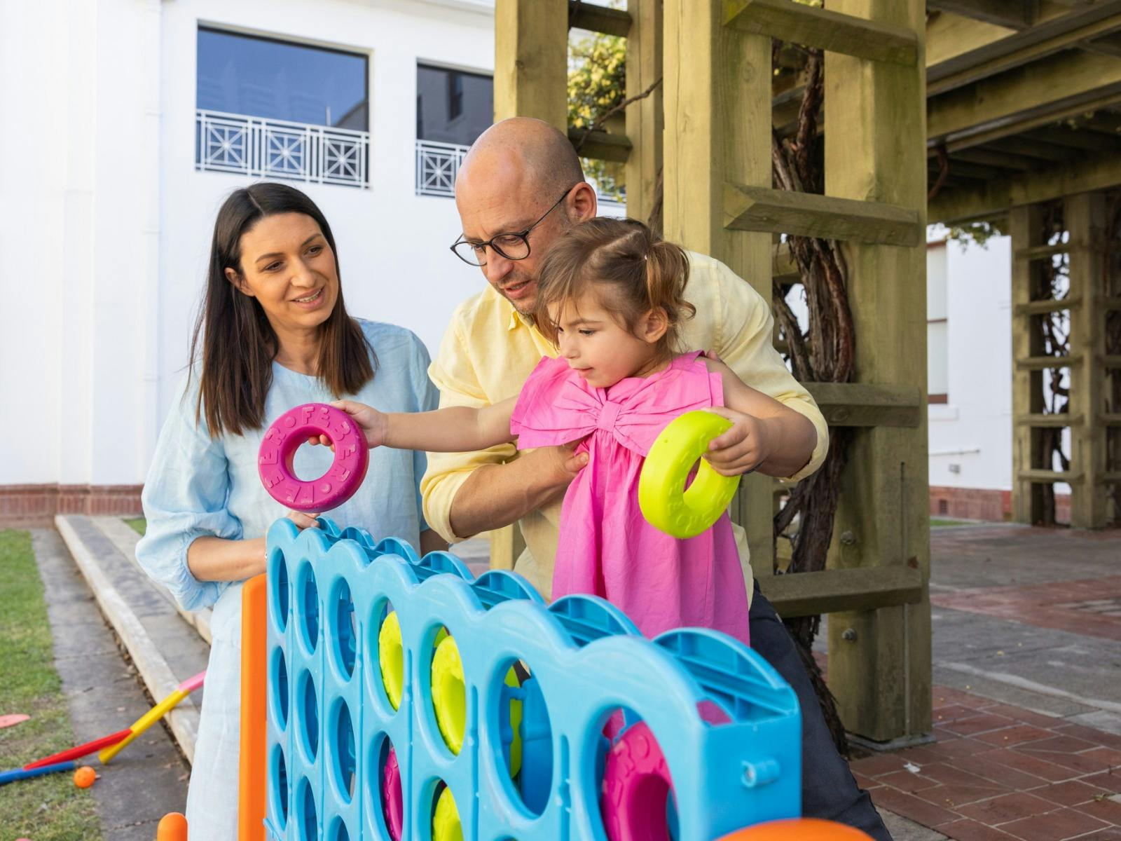 A father holding his young daughter while she places hoops into an oversized Tick-tack-toe game.