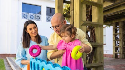 A father holding his young daughter while she places hoops into an oversized Tick-tack-toe game.