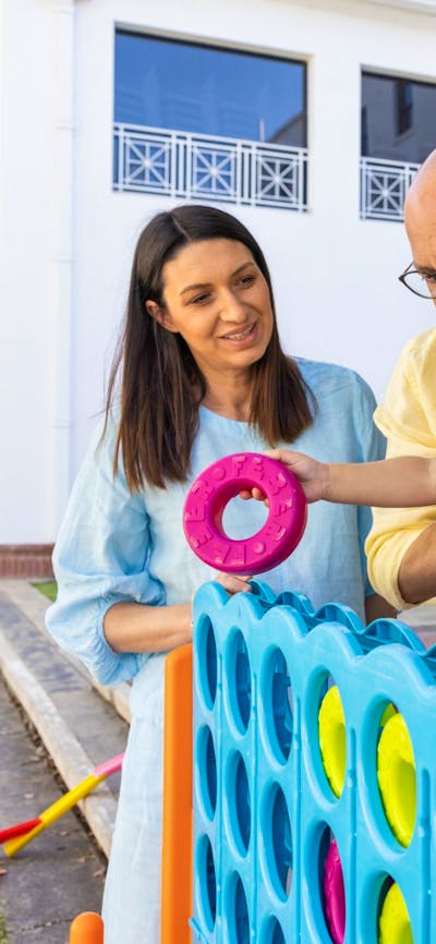 A father holding his young daughter while she places hoops into an oversized Tick-tack-toe game.
