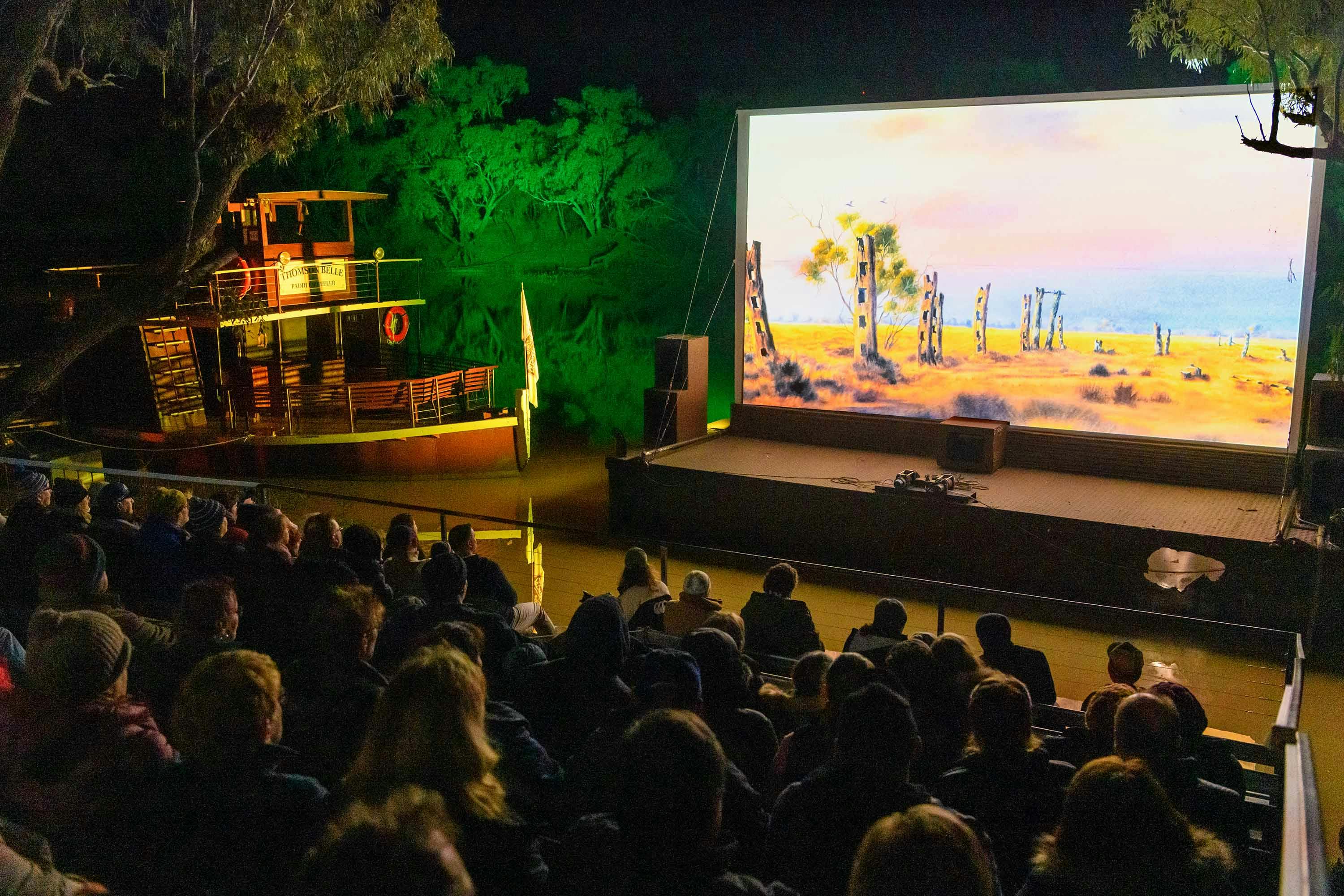 Illuminated river bank movie screen with guests watching at night