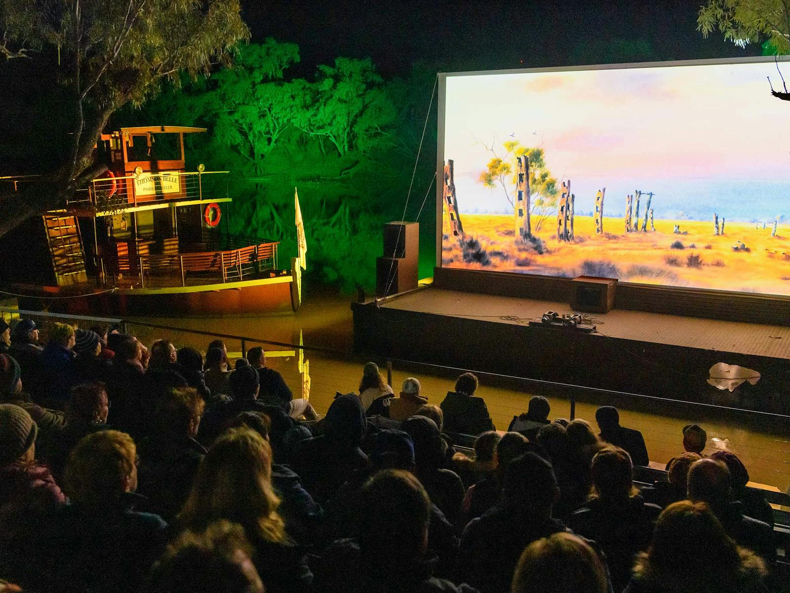 Illuminated river bank movie screen with guests watching at night