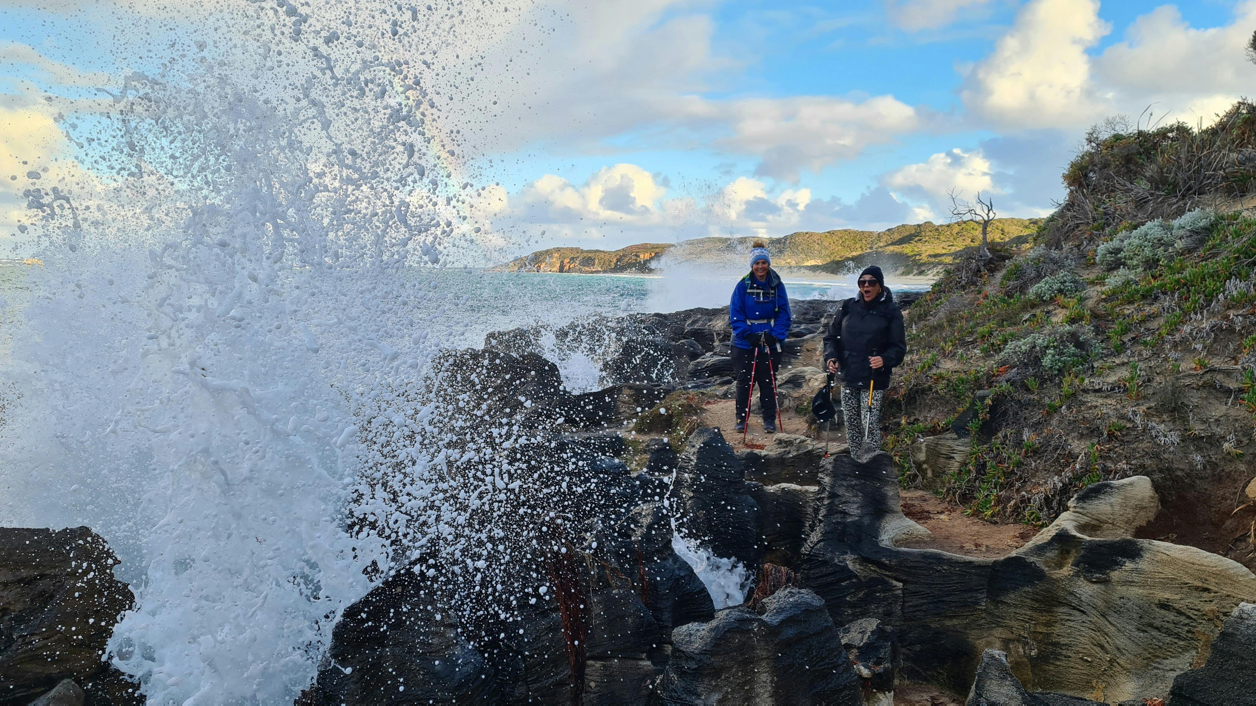 Hikers walking along coast with blow hole spurting water infront of them