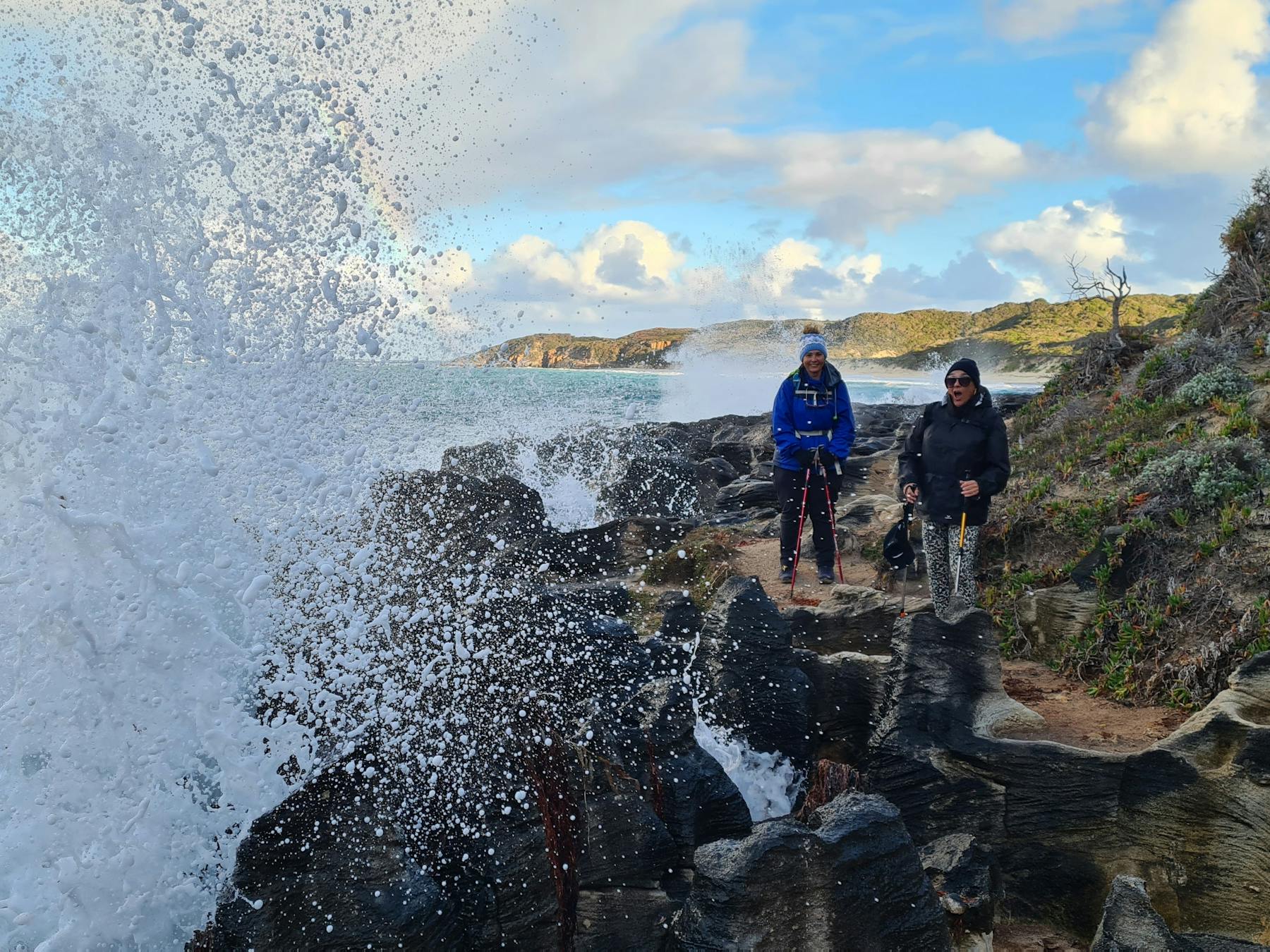 Hikers walking along coast with blow hole spurting water infront of them