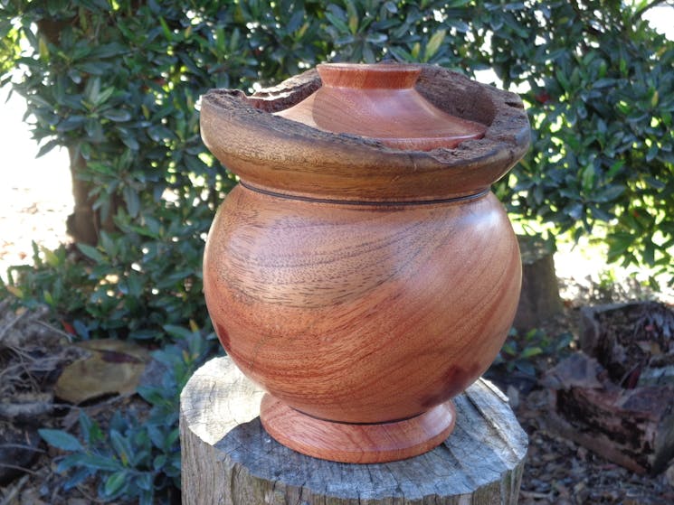 A dark timber urn with a natural finish sitting atop a log.
