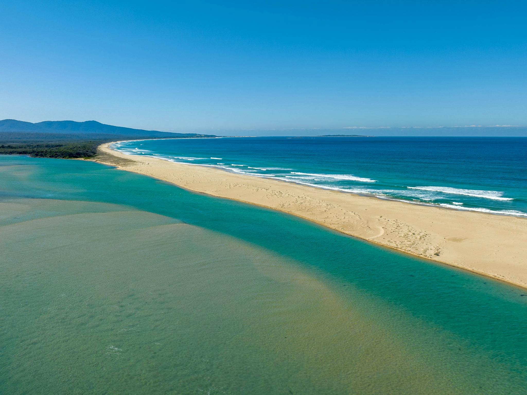 Sandy beachline with the sea on one side and inlet on the other