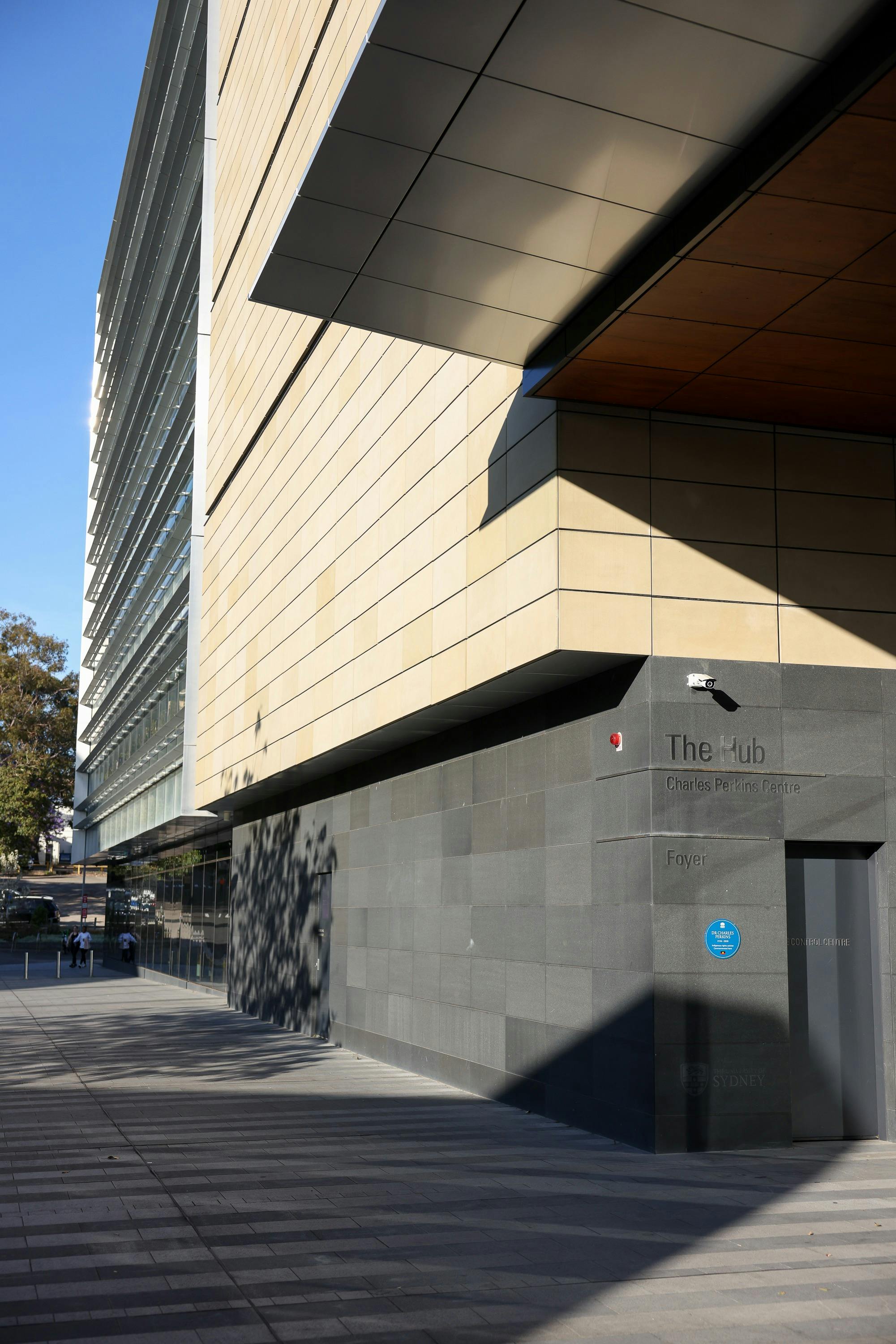 Blue plaque on wall of building  with signage above that says The Hub Charles Perkins Centre Foyer