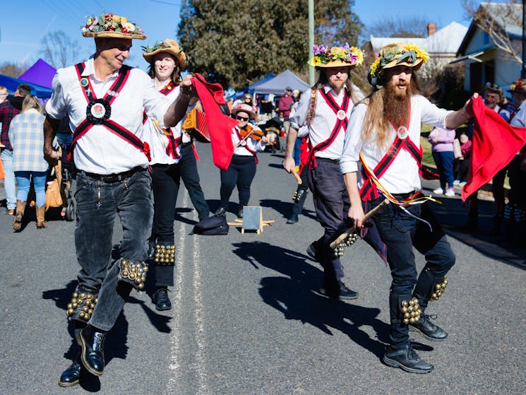 four dancers in white shirts, dark pants, braces and flowered hats