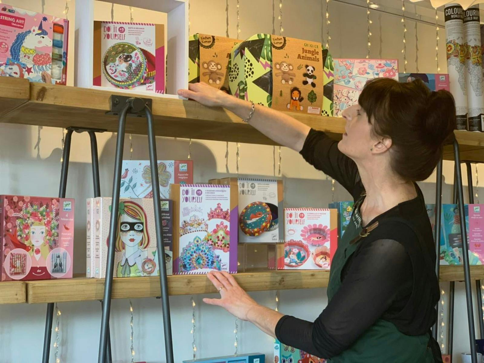 Nicola is the owner of the artHouse. She is reaching up arranging the products on the shelves