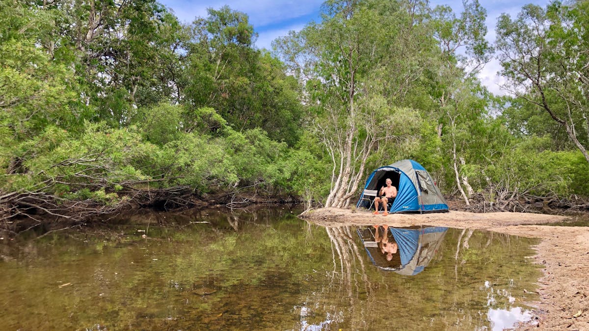 man sitting by tent next to creek