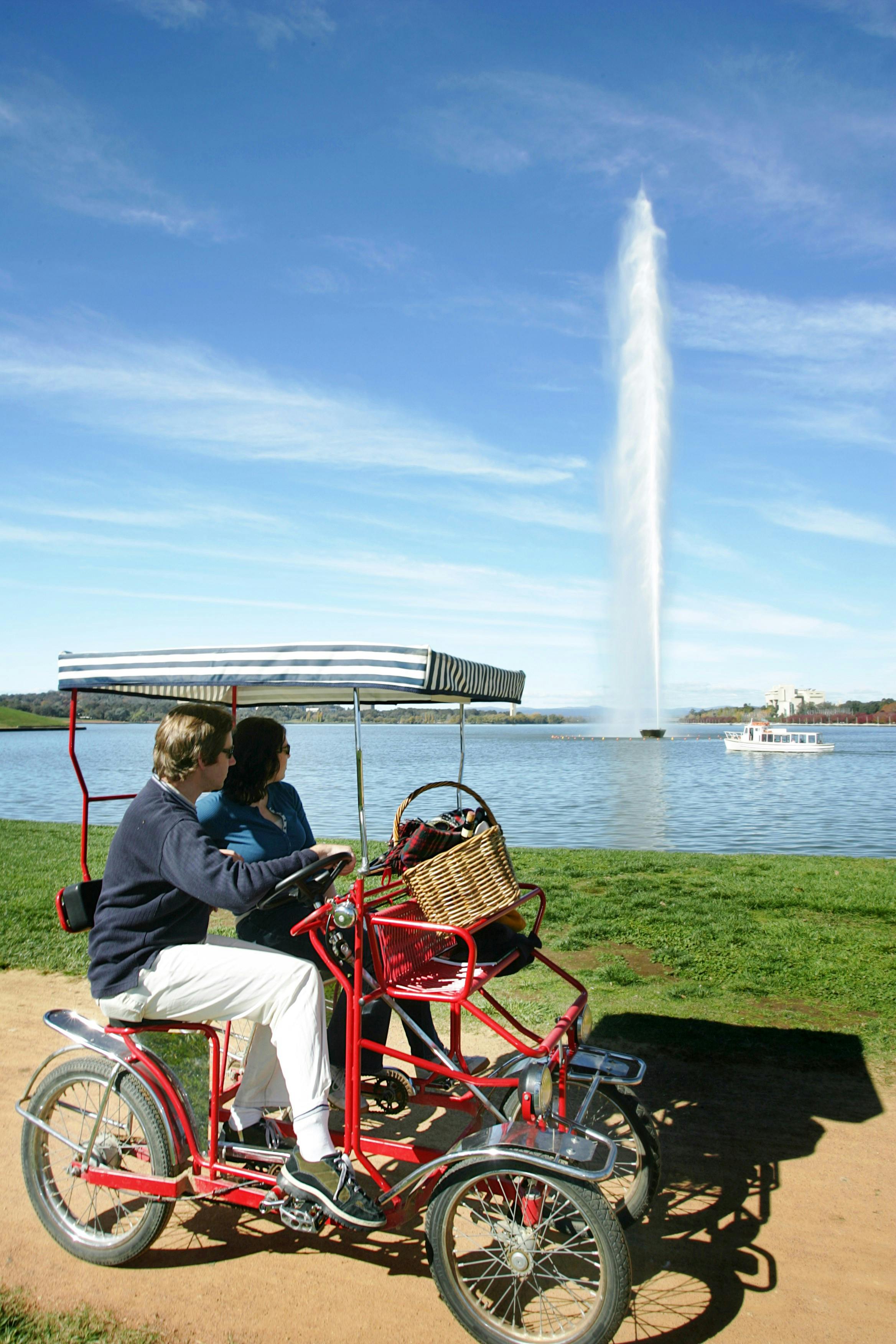 Couple cycling past Captain Cook Memorial Jet in Canberra