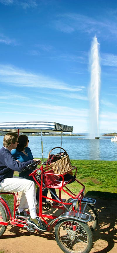Couple cycling past Captain Cook Memorial Jet in Canberra