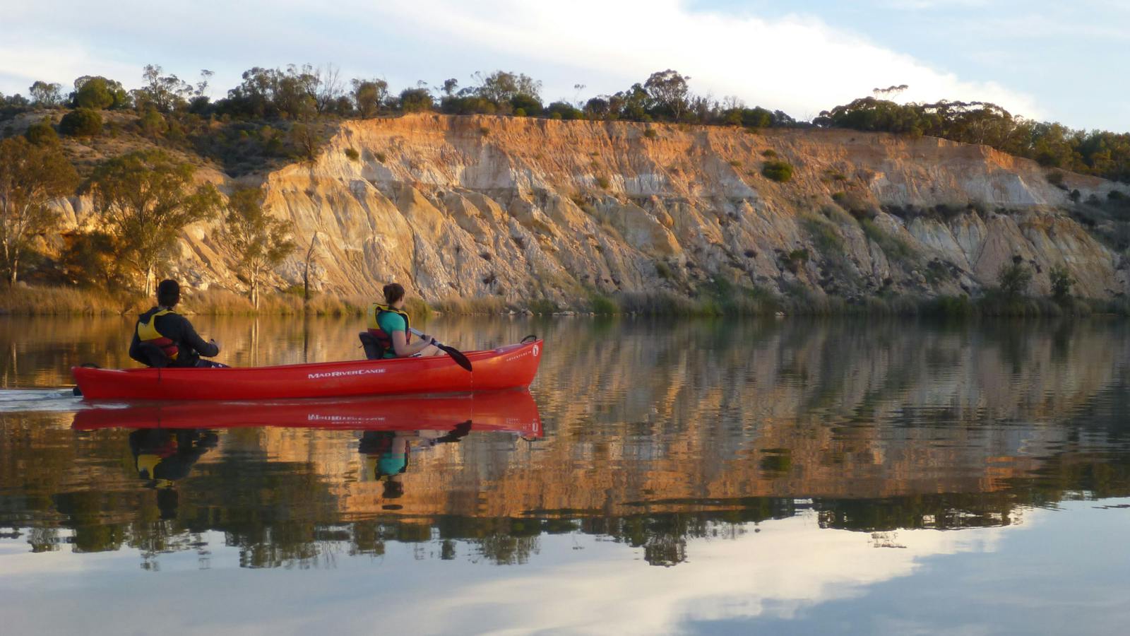 Paddlers in a double canoe glide past Bookpurnong Cliffs