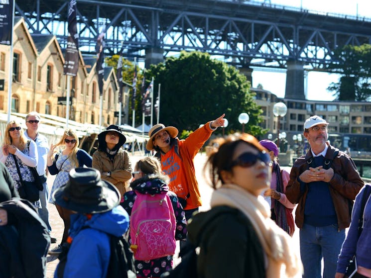 Sydney free walking tour near Sydney Harbour Bridge. A tour guide explains the history of the Rocks.
