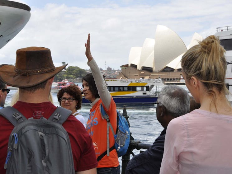 A tour guide in an orange uniform is leading free walking tour. Sydney Opera House in the background
