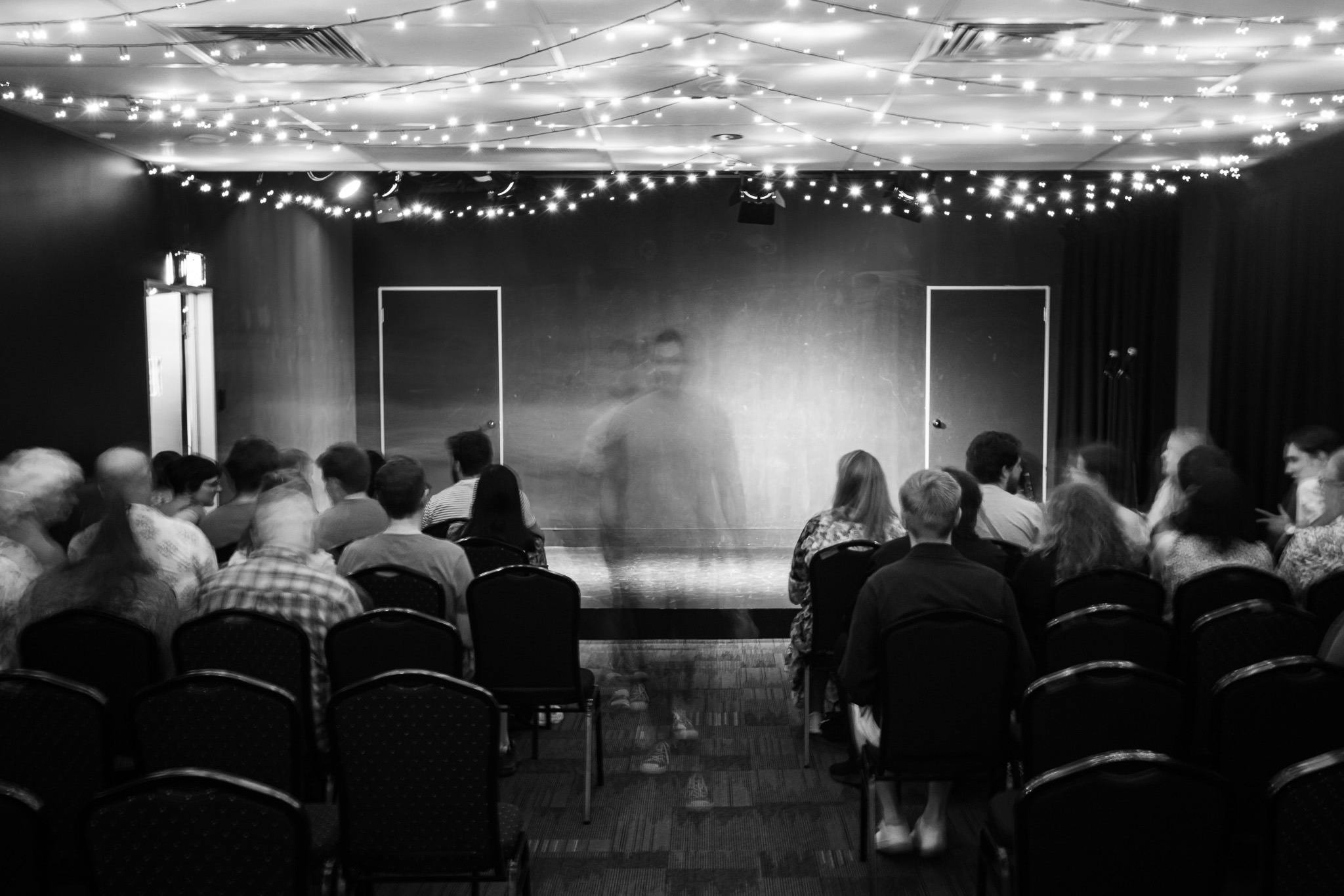 Black and white image of the theatre from back of room as people take their seats