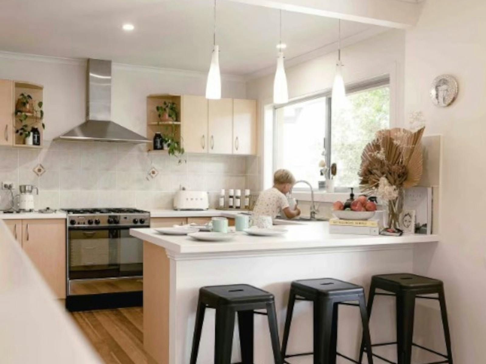 Beautiful white, light filled kitchen with large oven, sink and bench, bar stools and hanging lights