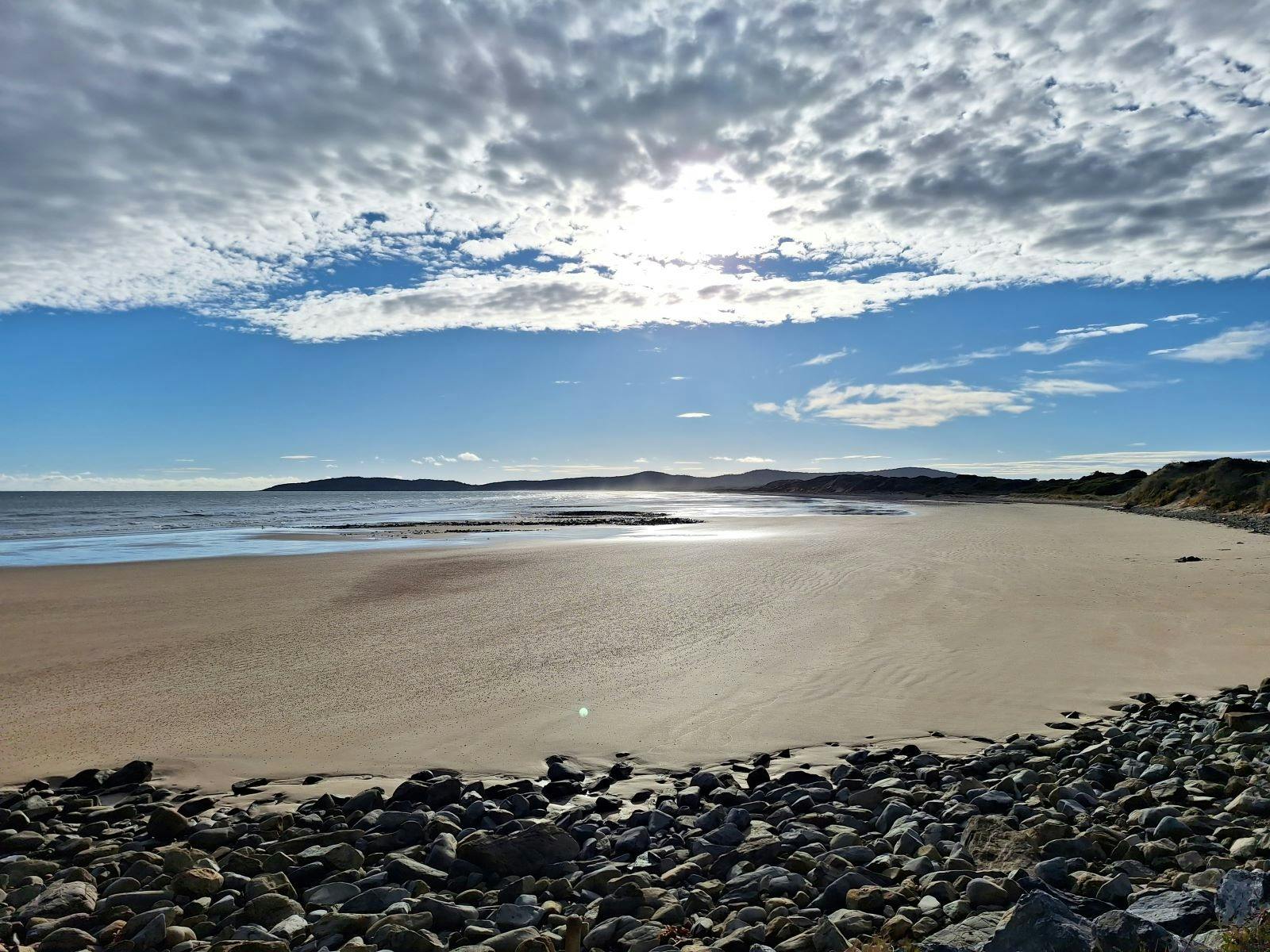 Beach with blue skies and white fluffy clouds with sunshine, sand and rocks