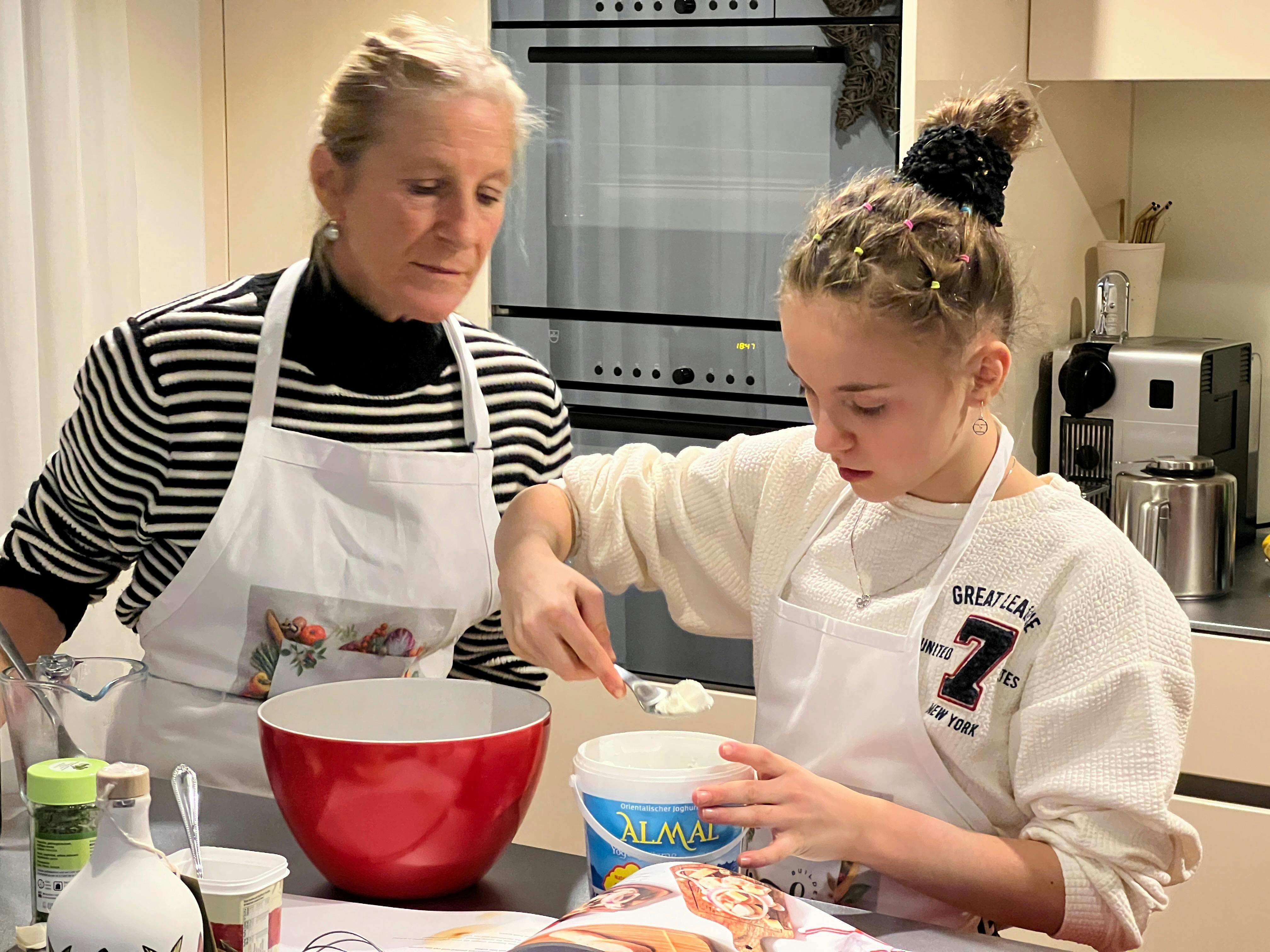 Anita Robin guiding a young participant as she measures ingredients during a baking class