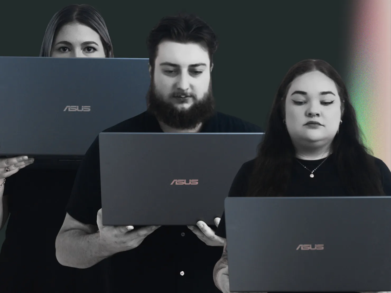 A male and two females stand holding a laptop each. The laptop is at different heights, hiding them.